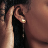 Dark-skinned model wearing a gold cat shaped drop earring.