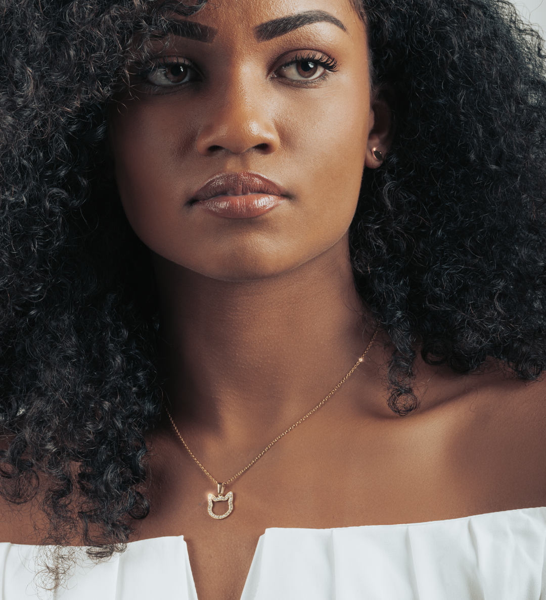 Beautiful dark skinned model wearing a necklace with sparkling cat head pendant in gold.