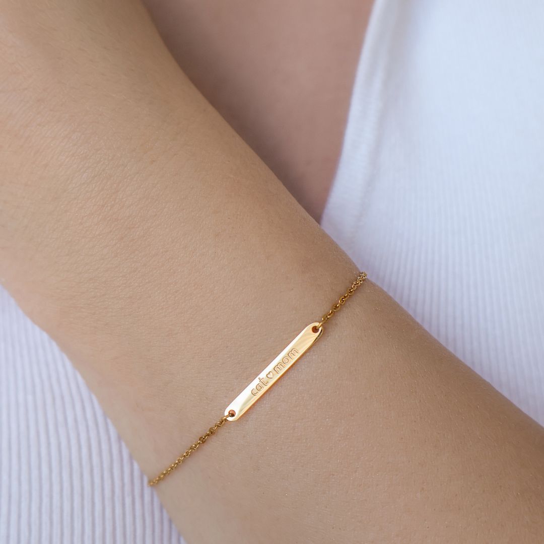A close up photo of model wearing a gold bracelet with sleek bar and engraved "cat mom" with heart letters.