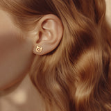 A model wearing gold stud earrings in the shape of cat head with little heart inside.