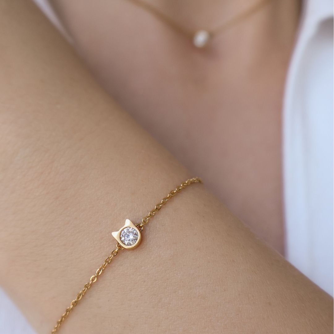 A close up image of model wearing a gold elegant bracelet with little cat shaped pendant and diamond in the middle.