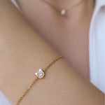 A close up image of model wearing a gold elegant bracelet with little cat shaped pendant and diamond in the middle.