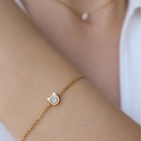 A close up image of model wearing a gold elegant bracelet with little cat shaped pendant and diamond in the middle.