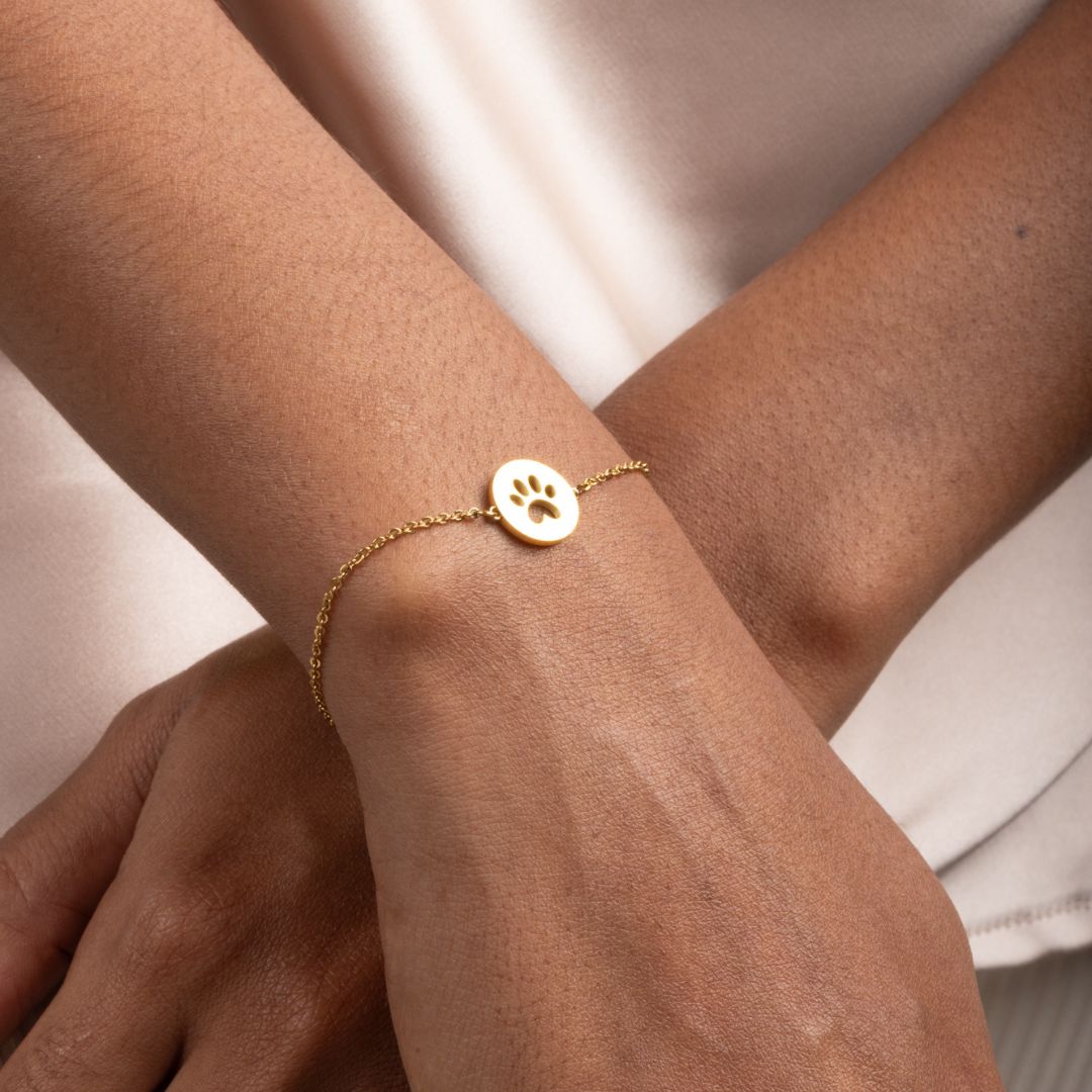 Close-up image of gold bracelet with round pendant that has paw print in the middle.