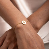 Close-up image of gold bracelet with round pendant that has paw print in the middle.