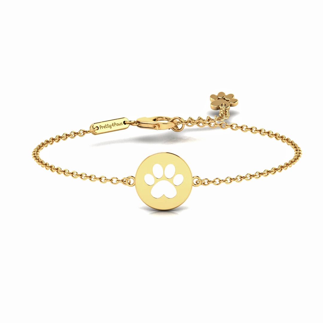 Product image of gold bracelet featuring elegant round pendant with cut-out paw print in the middle.