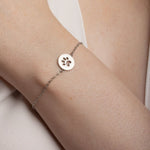 Close-up image of model wearing a stainless steel bracelet featuring round design with cat paw in the middle.