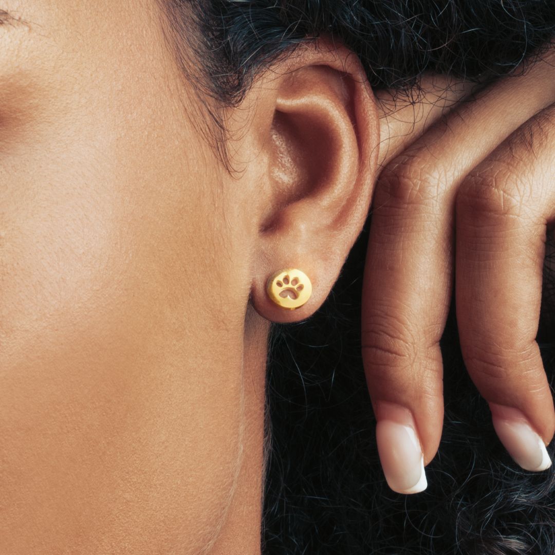 A dark-skinned model is wearing a round gold stud earring with the paw print in the middle.