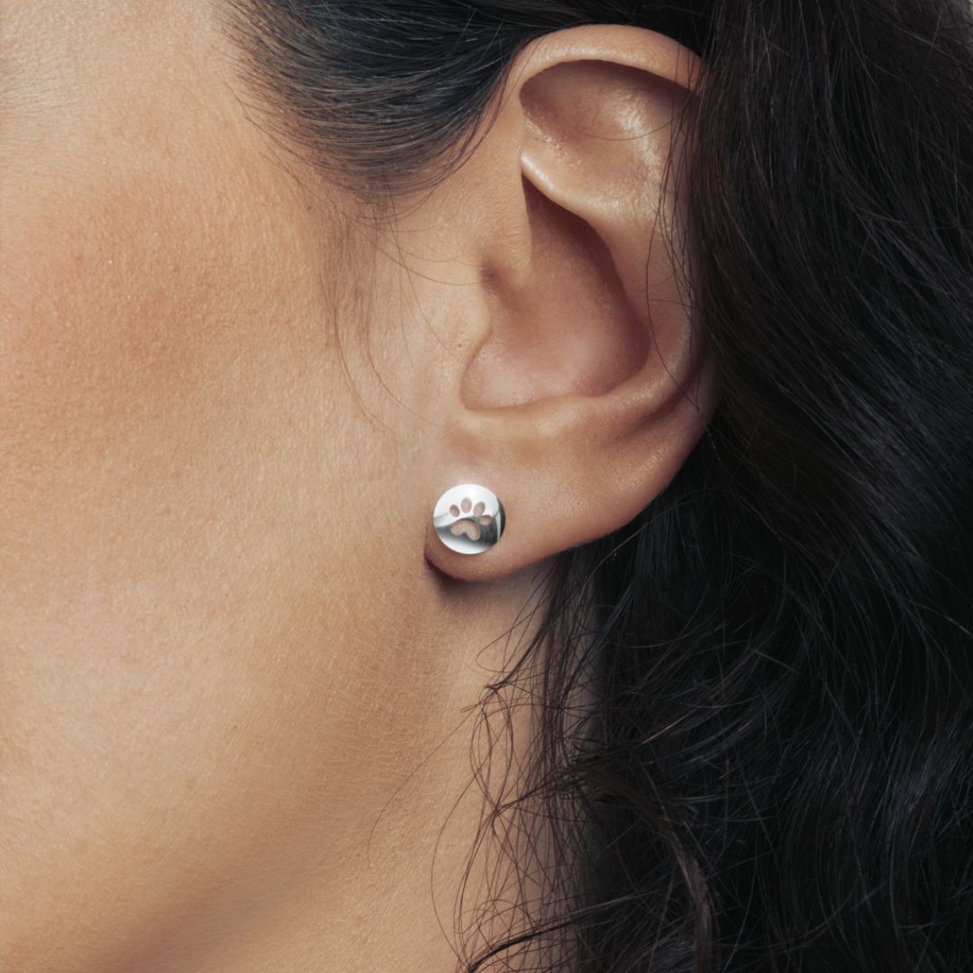 Model wearing a shiny silver round stud earring with the cat paw print inside.