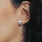Model wearing a shiny silver round stud earring with the cat paw print inside.