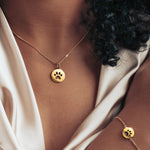 Gold paw print necklace and matching bracelet worn by a model, showcasing a coordinated and stylish look.