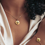 Gold paw print necklace and matching bracelet worn by a model, showcasing a coordinated and stylish look.