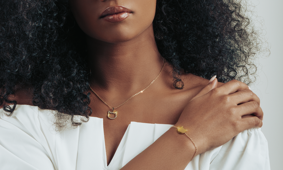 Model wearing a matching gold jewellery set including cat shaped necklace and bracelet.