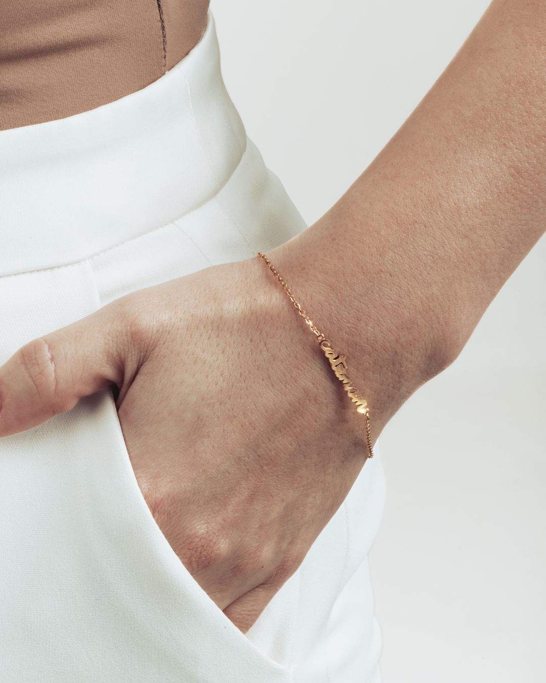 A hand in the pocket, visible gold cat mom letters bracelet. 