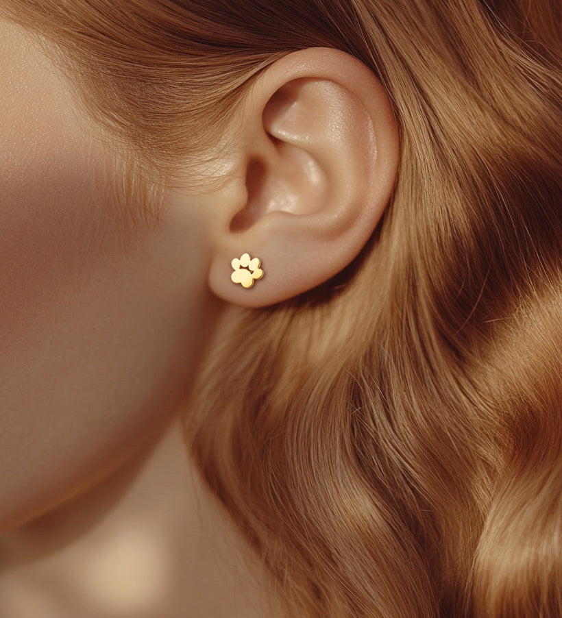 Close-up image of model wearing a gold paw shaped stud earring. 