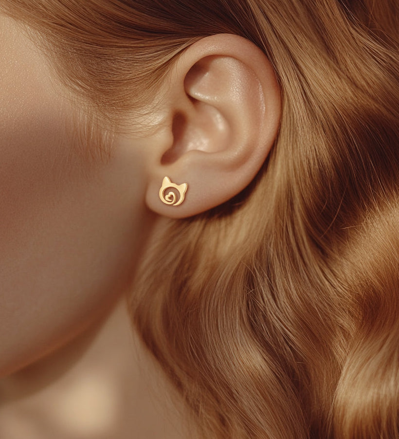 A model wearing gold stud earrings in the shape of cat head with little heart inside. 
