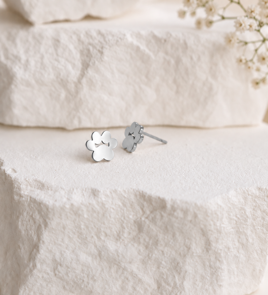 18K gold-plated stainless steel paw stud earrings on textured ivory stone with delicate baby’s breath flowers.