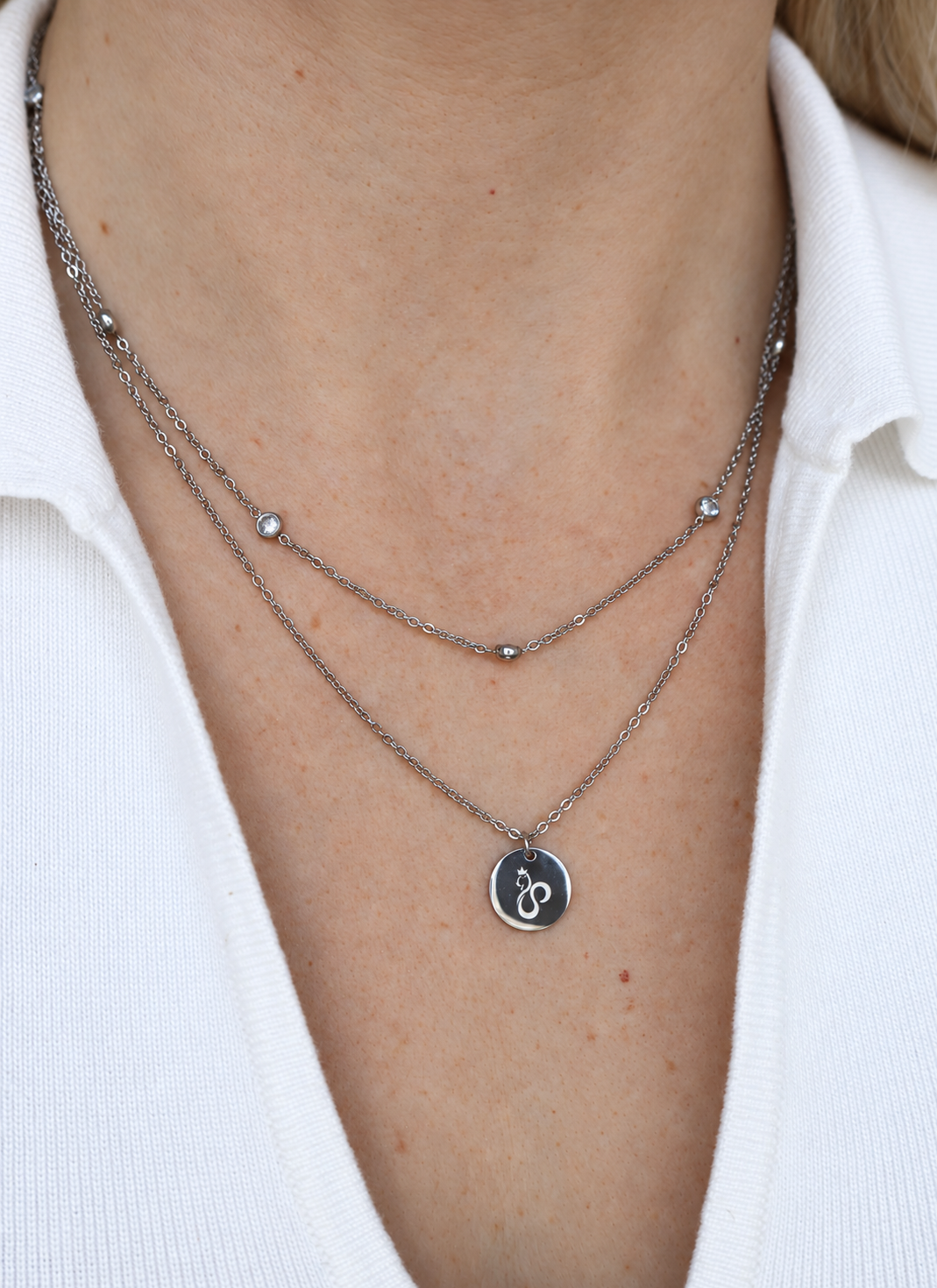 Double layer cat necklace worn with an open white shirt, showing the sparkling upper chain and round signature cat pendant.