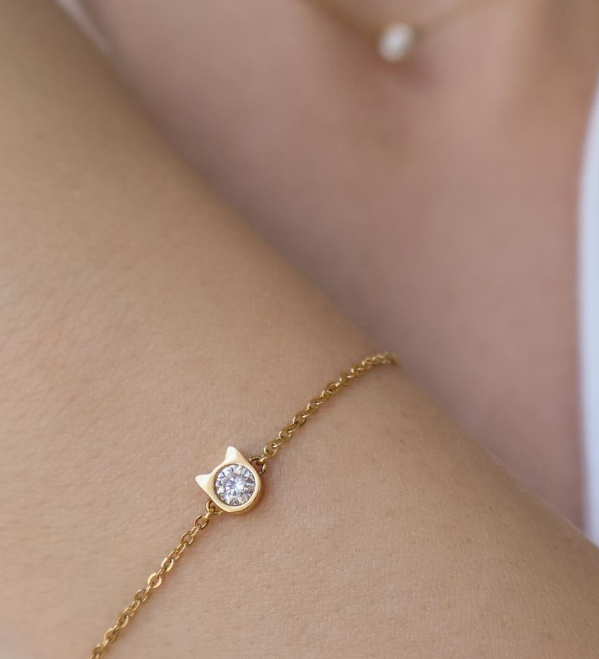 A close up image of model wearing a gold elegant bracelet with little cat shaped pendant and diamond in the middle. 