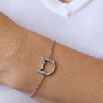 A stainless steel chain bracelet with a cat head charm paved with small zircon stones, shown worn on a person's wrist against a white shirt background.