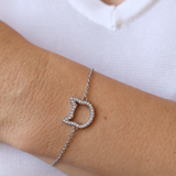 A stainless steel chain bracelet with a cat head charm paved with small zircon stones, shown worn on a person's wrist against a white shirt background.